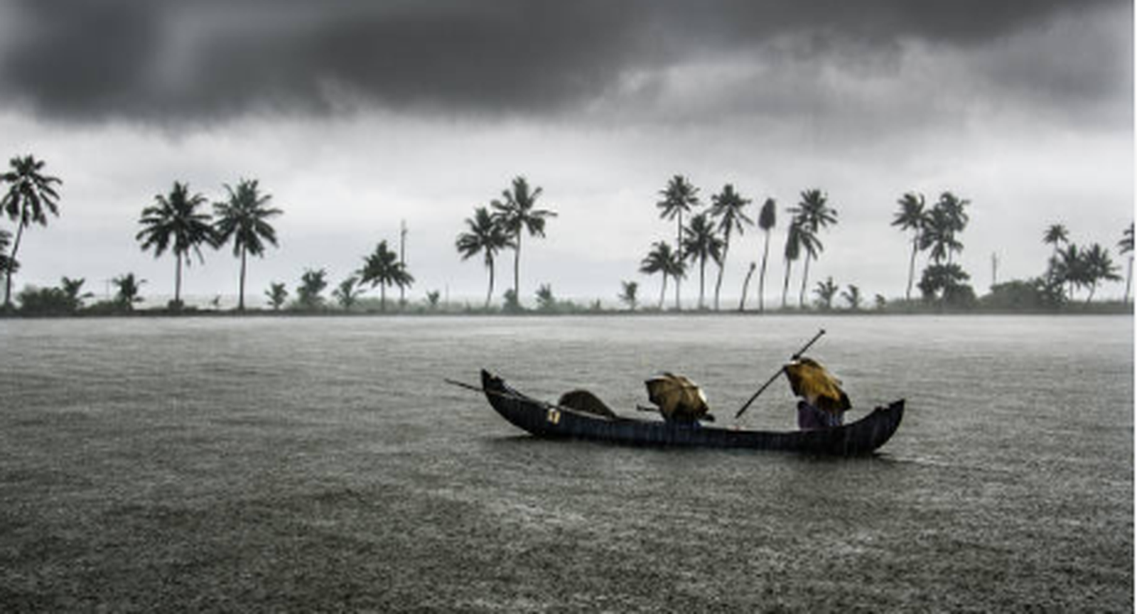 Traditional wooden boat carrying people across Kerala backwaters beneath dark monsoon clouds, with coconut palms lining the distant shore.